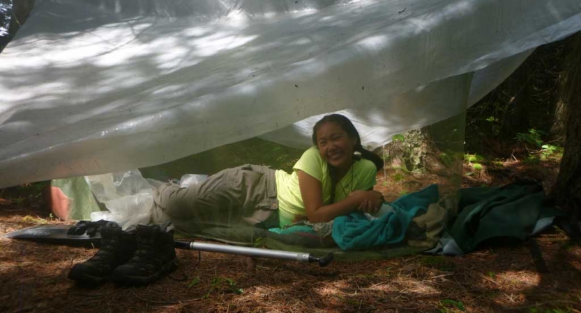 a person smiles from under a tarp shelter on an outward bound course